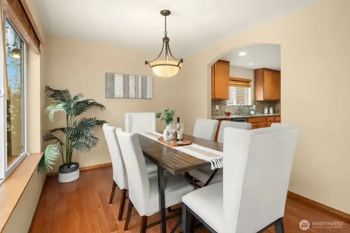 This alternate view of the dining room further showcases the warm and inviting atmosphere created by the elegant chandelier, rich hardwood floors, and the bright window framing lovely views of the surrounding greenery. The seamless sightline through to the kitchen beyond perfectly illustrates the open and connected flow of the main level layout.
