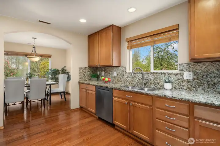 This well-appointed kitchen features warm wood cabinetry extending to the ceiling for maximum storage, gleaming granite countertops, a brand new stainless steel oven range, and a large window above the sink that fills the space with natural light. The polished finishes, hardwood floors, and open sightline to the dining area create a cohesive and elevated feel that makes this kitchen as functional as it is beautiful.