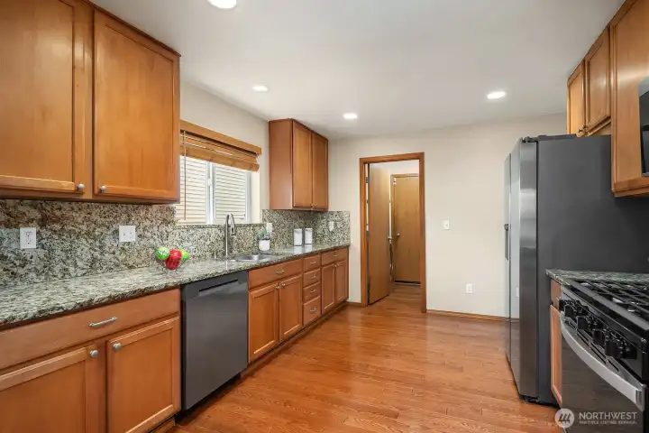 This wide view of the kitchen showcases the full scope of the space, featuring ceiling-high cabinetry on every wall for truly exceptional storage, gleaming granite countertops, a beautiful tile backsplash, and a full suite of stainless steel appliances. The hardwood floors, recessed lighting, and cohesive polished finishes throughout make this a kitchen that is as practical and organized as it is stylish.