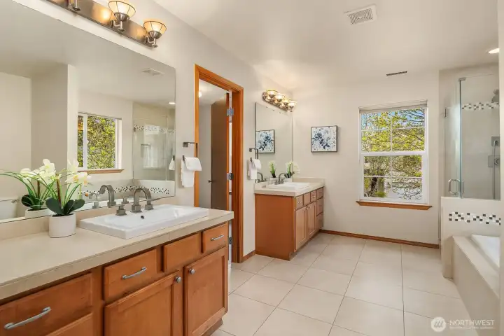 The spa-inspired primary bath features dual vanities with warm wood cabinetry, a sunken soaking tub, and a sun-drenched window — a luxurious escape with every detail thoughtfully appointed.