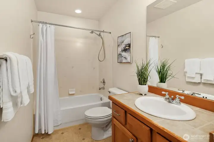 A clean and well-appointed full bath featuring warm wood cabinetry, a tub/shower combo, and classic finishes — thoughtfully designed to serve the additional bedrooms with ease.