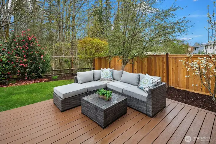 The expansive wood deck is the perfect outdoor living space, complete with a stylish sectional seating area surrounded by lush greenery — ideal for entertaining or simply unwinding in the fresh air.