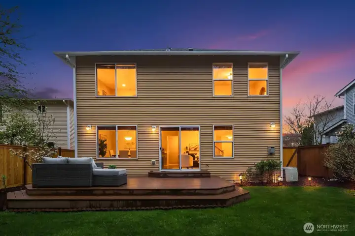 Another breathtaking dusk view highlighting the home's impressive back elevation, large windows radiating warmth, and the inviting deck and patio space — a truly magical setting to come home to.