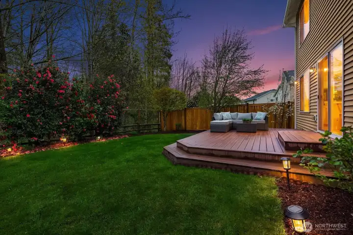 A magical dusk view of the beautifully landscaped backyard, with soft landscape lighting illuminating the lush lawn and deck — creating a warm and enchanting outdoor ambiance perfect for evening entertaining.