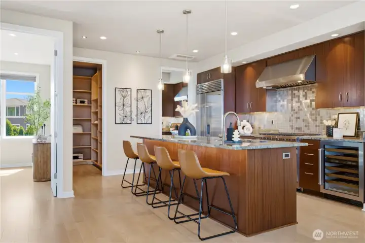 A waterfall-edge island that seats four, a wine fridge, and a walk-in pantry with custom shelving — the heart of the home, fully equipped.