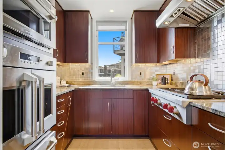 Professional-grade kitchen featuring Wolf gas stove, double wall ovens, Sapele wood cabinetry, stone counters, and mosaic tile backsplash.