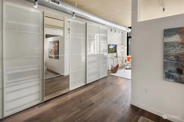 The built-in storage with frosted glass sliding doors and a full-length mirror adds a modern, clean aesthetic while offering ample space to organize and store belongings. Perfect for maximizing functionality without sacrificing style in this open loft layout.