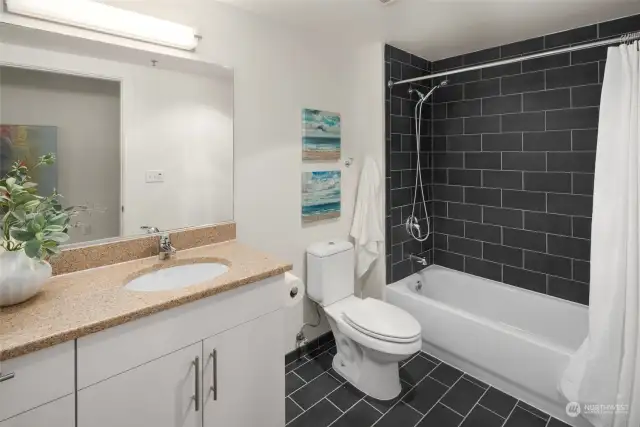 The sleek bathroom features dark tile accents, a full-sized tub, and a spacious vanity with plenty of storage, providing both comfort and functionality in a contemporary design.