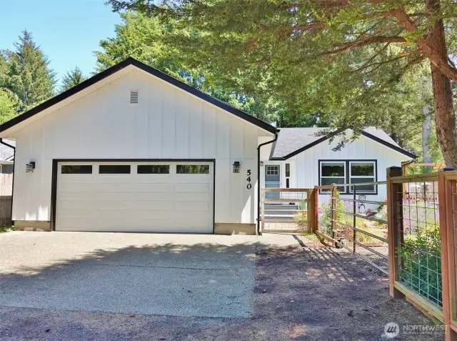 Front of the home w/ driveway and 2-car garage and a large side gate into the front yard.