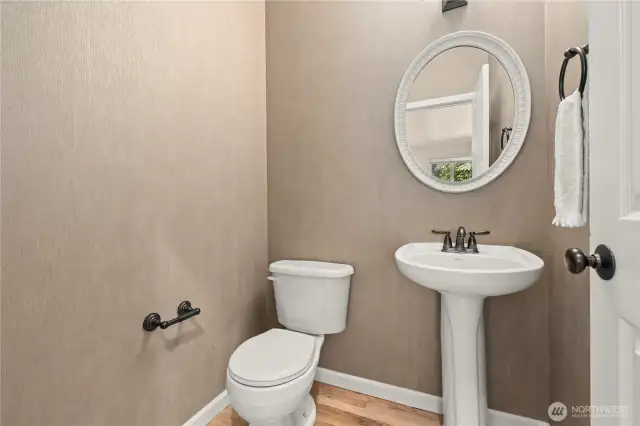 This stylish half bathroom is ideally located on the main floor of this Puyallup, WA home, just steps from both living rooms, the kitchen, and formal dining area. Featuring a classic pedestal sink, oil-rubbed bronze fixtures, and a round framed mirror, the space offers both function and charm. Neutral-toned wallpaper and hardwood floors add a refined touch. Perfect for guests, this powder room is a thoughtful and practical addition to the home’s well-planned layout in the heart of the LaGrande Station community.