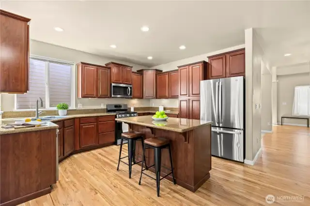 This sun-filled kitchen in Puyallup’s LaGrande Station community offers timeless design and modern convenience. Rich wood cabinetry, granite countertops, and a central island with bar seating create a stylish and functional workspace. Stainless steel appliances, a gas range, and under-cabinet lighting complete the chef-ready setup. Multiple windows and a sliding glass door flood the space with natural light and offer serene greenbelt views from the cozy breakfast nook. With easy access to the backyard and adjacent living areas, this kitchen is the heart of the home in one of Puyallup, WA’s most desirable neighborhoods.