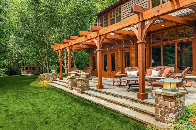 Exterior stone terrace off of living room spans the width of the home and continues the arches theme with the handcrafted wood trellis.