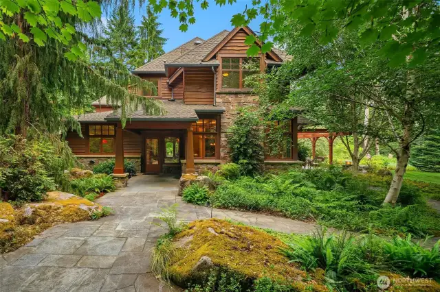 View of the home from the south showcasing the massive rocks “planted” by the landscaper and the stone walkways lining the lush greenery.