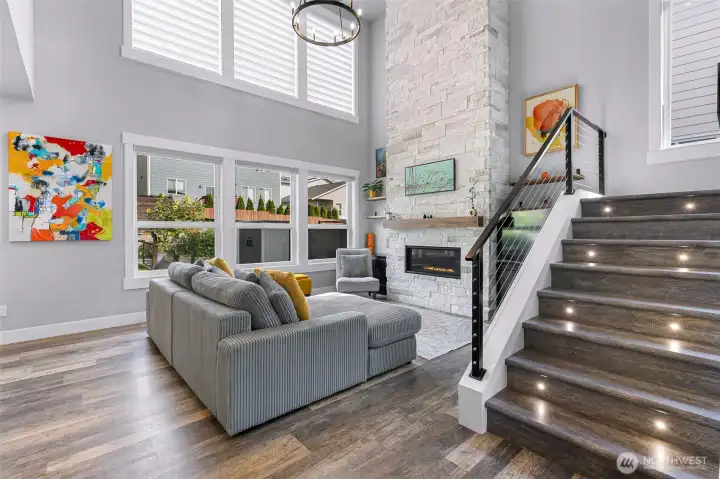 Large living room with vaulted ceilings, stone fireplace, and a wall of windows with custom blinds.