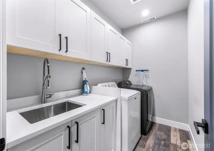Upstairs laundry room with utility sink and quartz counters.