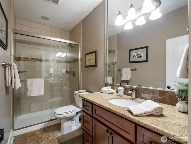 Hall bath with travertine tile floors, single vanity with granite countertop and shower with tile surround.