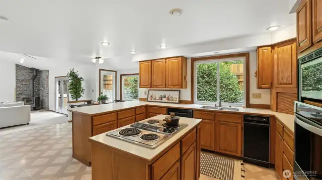 Enjoy a bright, open-concept kitchen featuring ample counter space, a center cooktop island, and modern can lighting—all seamlessly connected to the cozy family room with a wood-burning stove