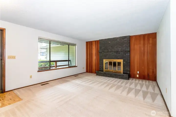 Large living room, accented by fireplace and large east-facing front windows, front door to far left.