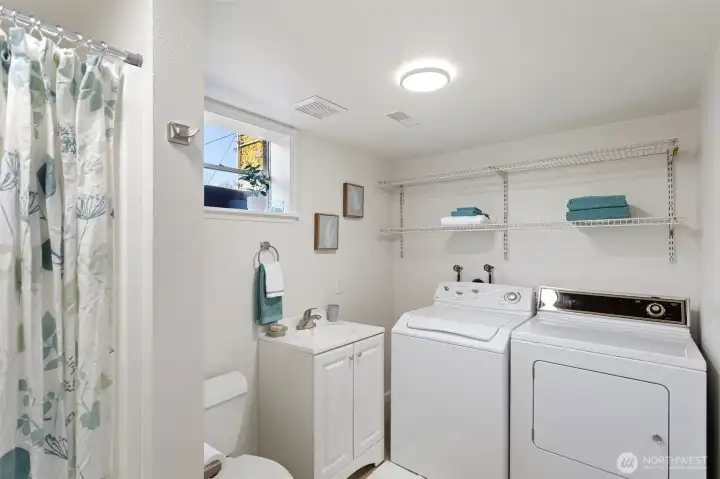 Updated lower-level ¾ bath with integrated laundry, featuring a refreshed vanity, LVP flooring, updated lighting, and natural light from a window. Clean and functional, with washer and dryer included.