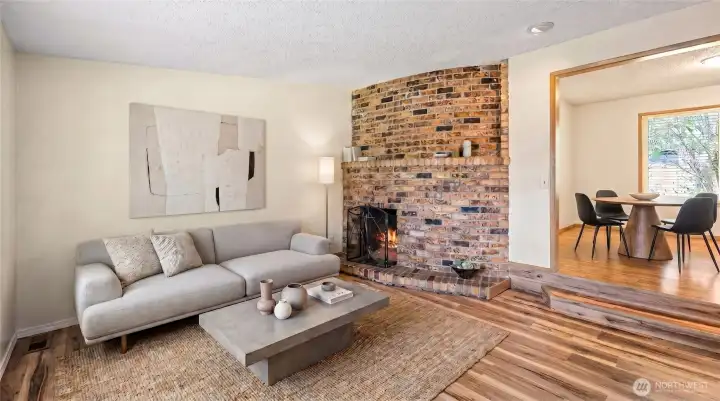 Living room with Lovely rounded brick fireplace that has electrical outlets for TV built in above, so no need to have long extensions hanging down to a plug. Virtually staged