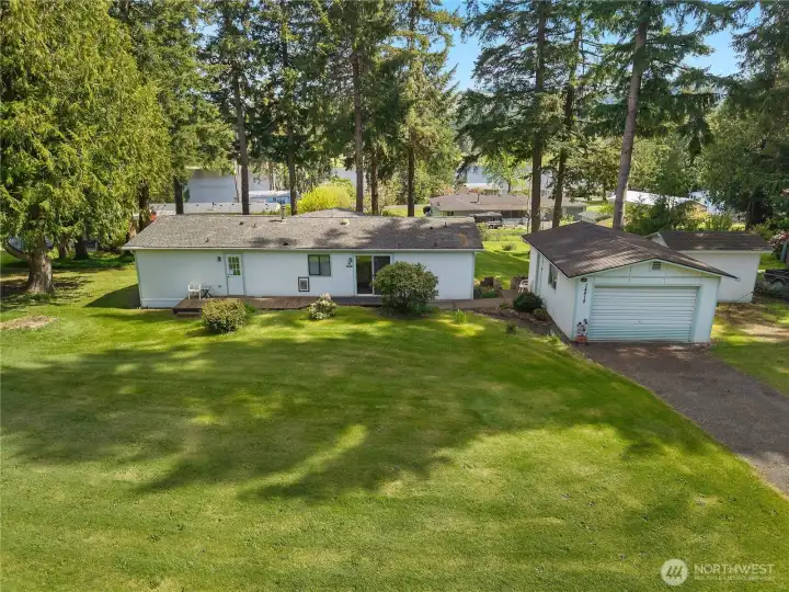 Aerial view shows the home, garage, broad yard, mature evergreens, and nearby lake setting.