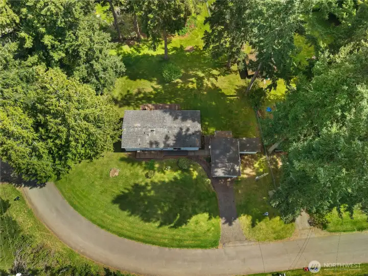 Overhead perspective shows the home’s layout, yard space, driveway, and wooded surroundings.