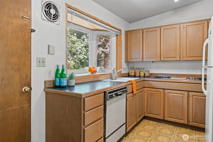 The kitchen features solid wood cabinetry, a garden window above the sink, and a functional L-shaped layout with plenty of storage. This is a great candidate for a kitchen remodel — the footprint is right, the cabinet count is strong, and the natural light is already there.