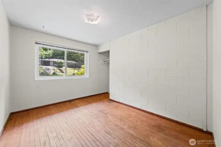 Bedroom 1 features hardwood floors, a garden-view window, and an exposed painted brick accent wall that gives it real character. A blank slate for a home office, workout room, or guest bedroom — flexible space in one of Bellevue WA's best-value neighborhoods for buyers on the Eastside.