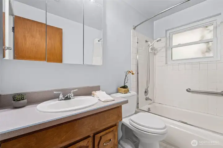 The full bathroom features a tub-shower combo with white tile surround, a wide vanity with wood cabinetry, and a medicine cabinet with mirror — clean, functional, and ready to use while you plan your updates.
