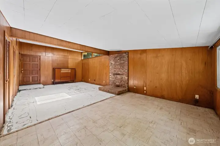 Another angle of the spacious rec room in this Eastgate Bellevue WA fixer — showing the full depth of the space, the second brick fireplace with raised hearth, warm wood-paneled walls, and clerestory windows that bring in natural light.