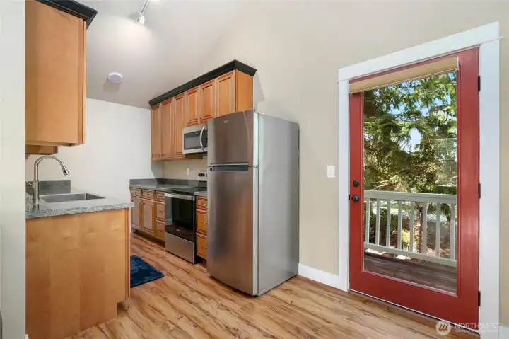 Another view of view of kitchen in apartment above garage. Glass storefront door to deck outside.