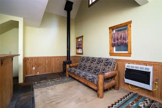 Step inside to vaulted ceilings in the living room with slate flooring and a corner wood stove. Propane wall heater provides an additional source of heat.