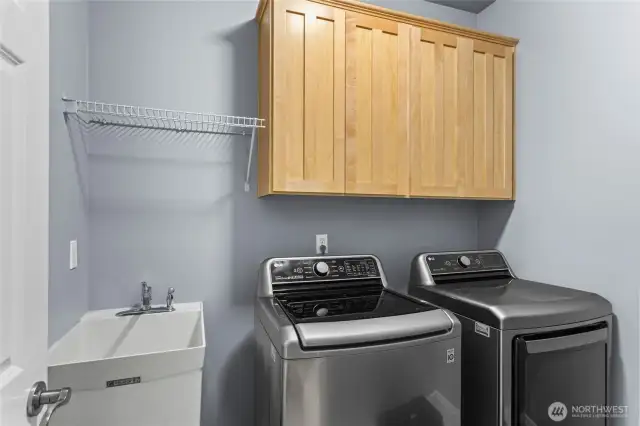 A utility sink, a hanging shelf, and additional cabinetry enhance the appeal of this laundry room.