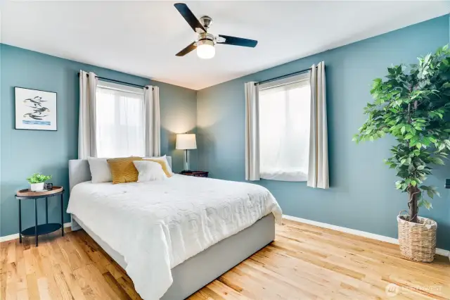 This primary bedroom features natural light from large windows, newer refinished hardwoods and ceiling fan to keep the air from your newer heat pump moving!