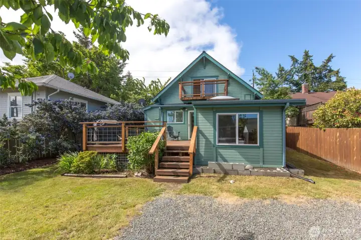 The backyard view showcases the rear of the blue character home, complete with a small lawn, wooden steps, and a gravel workspace.