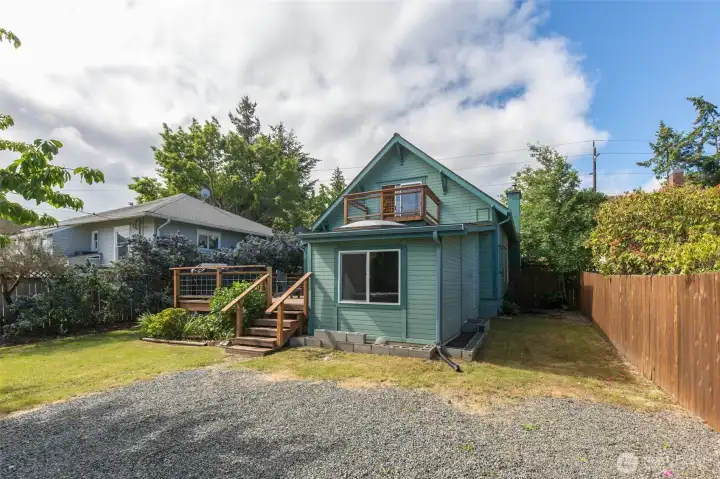 An angled rear shot highlights the back of the house, a wooden privacy fence, and the spacious off-alley gravel parking area.
