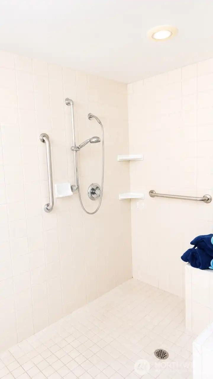 Gigantic roll-in tiled shower with grab bars and quality fixtures.