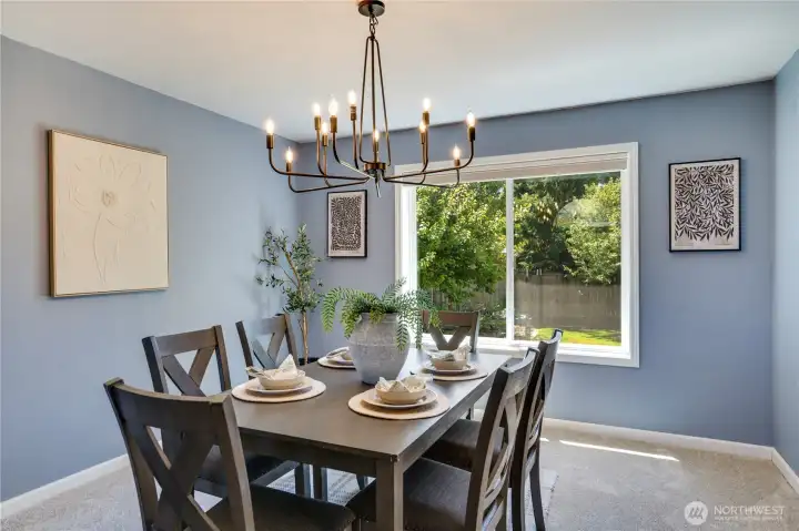 A large picture window overlooking the backyard brightens the formal dining room, where new main-floor baseboards and an updated light fixture (2026) give the space a fresh, finished look.