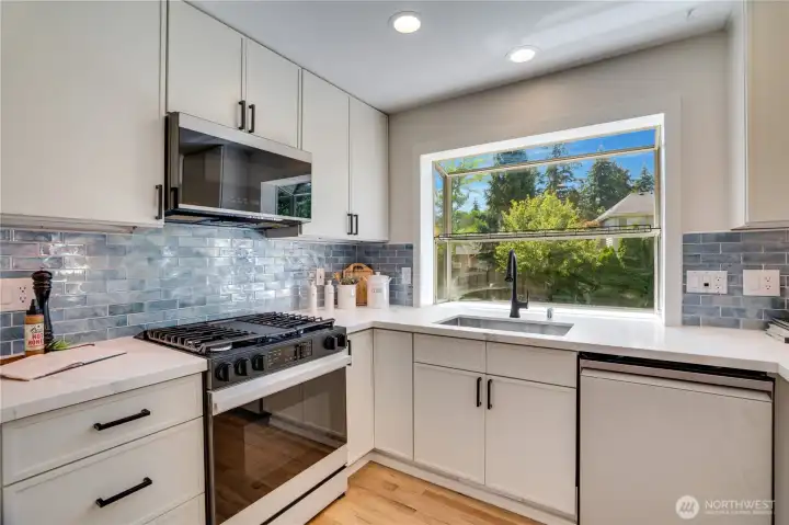 Natural light pours through the oversized window above the sink, highlighting the glossy stacked subway tile backsplash, updated fixtures, and new appliances completed during the 2025 remodel.