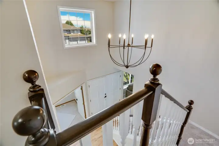 The open upper landing overlooks the two-story foyer below, where a dramatic chandelier and oversized window continue to fill the home with natural light.