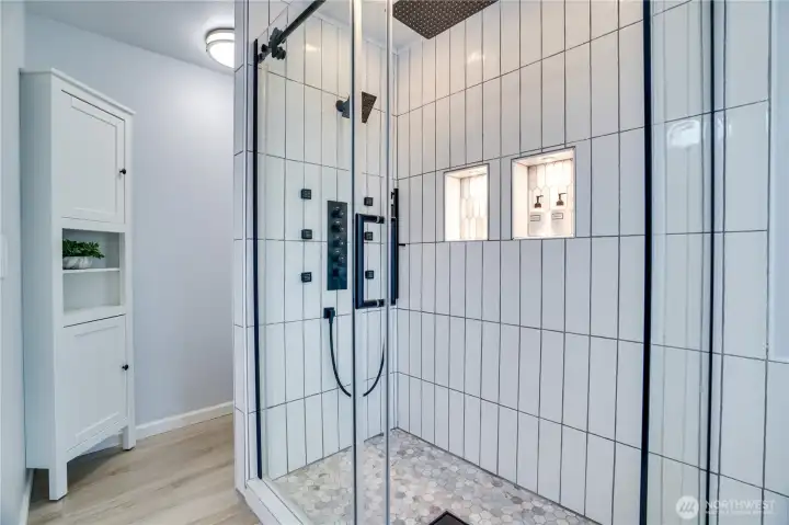 The spacious tiled shower showcases dual showerheads, body sprays, built-in niches, and frameless glass that elevate the daily routine.