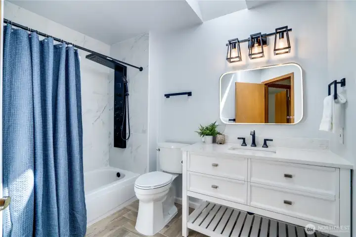 The updated hall bath features a modern vanity, illuminated mirror, and stylish tub/shower with contemporary tile and black fixtures.