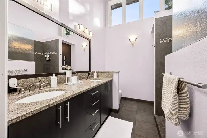 The fully remodeled primary offers a generous two sink vanity grooming space, extra storage, a "Toto" style commode/bidet and gian walk-in tiled shower with glass half-wall,  all appointed in rich natural tones.