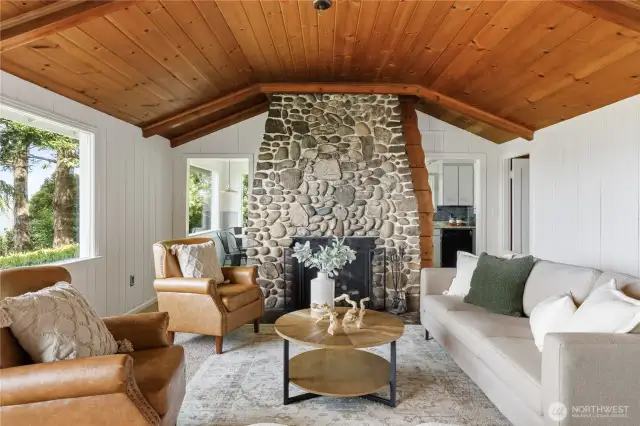 Warm and inviting living room with a stunning river rock fireplace, wood-paneled ceiling, and sound views—cozy island charm at its finest.