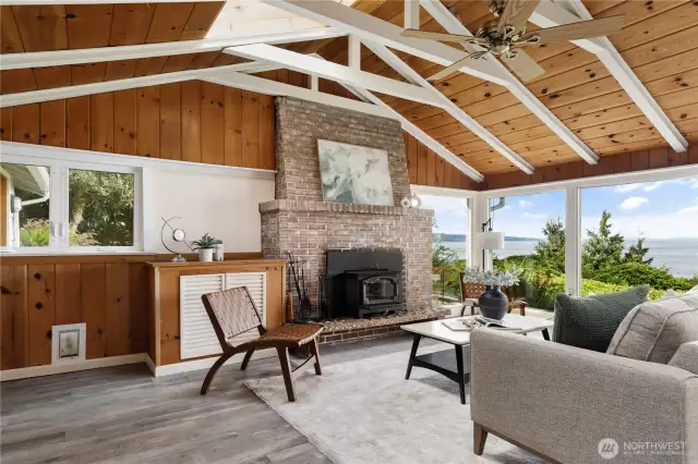 Charming wood-paneled living room with vaulted ceilings and cozy wood stove, all framed by stunning sound views.