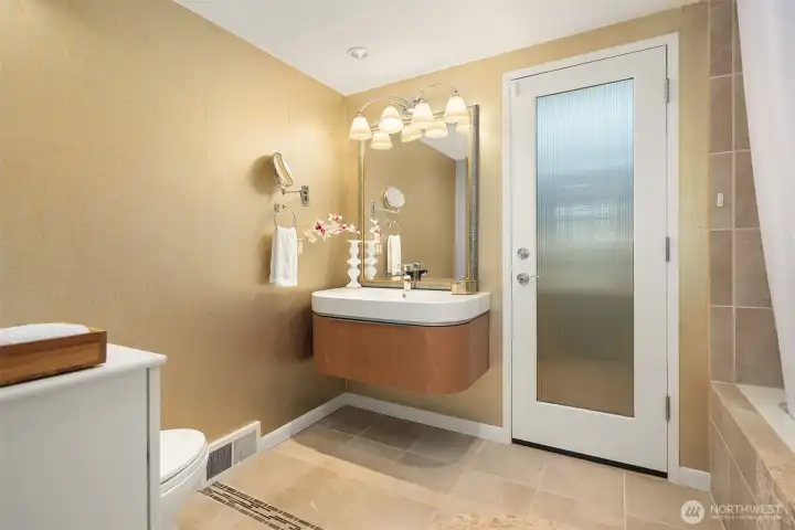 A privacy-diffused glass door opens from the primary bath to the back/side patio with planting beds, and welcomes soft light into the room.