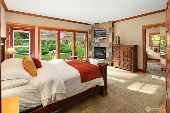 Spacious primary suite with attached TV, cozy gas fireplace, large picture windows, and en-suite 5 piece bath