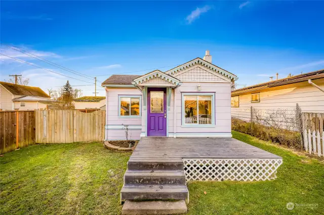 This alternate angle of the front exterior highlights the spacious yard and the home’s charming design details. The vibrant purple door and decorative trim add a touch of personality, while the fenced yard offers privacy and potential for landscaping.