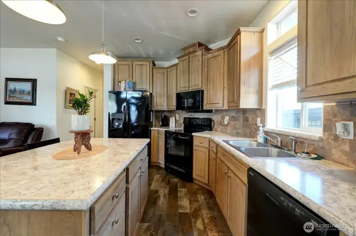 Step into a kitchen that's both beautiful and functional. Featuring warm, natural wood cabinets and stunning speckled countertops, this space offers a large island with seating, perfect for casual meals or entertaining guests. Modern black appliances and a stylish tile backsplash complete the look, making it a true centerpiece of the home. This kitchen is a must-see for anyone who loves to cook and gather.