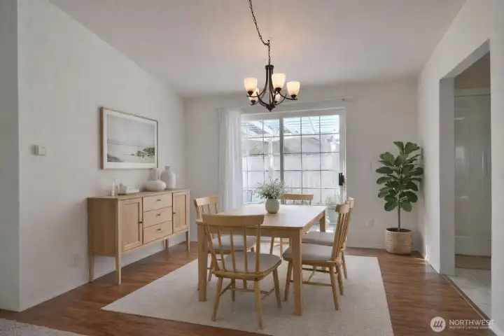 Dining room with vaulted ceiling, laminate flooring, and a sliding door that leads to a private back patio.  virtually staged.